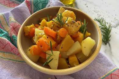 Yellow bowl filled with carrot, potato and pumpkin cubes topped with rosemary spring