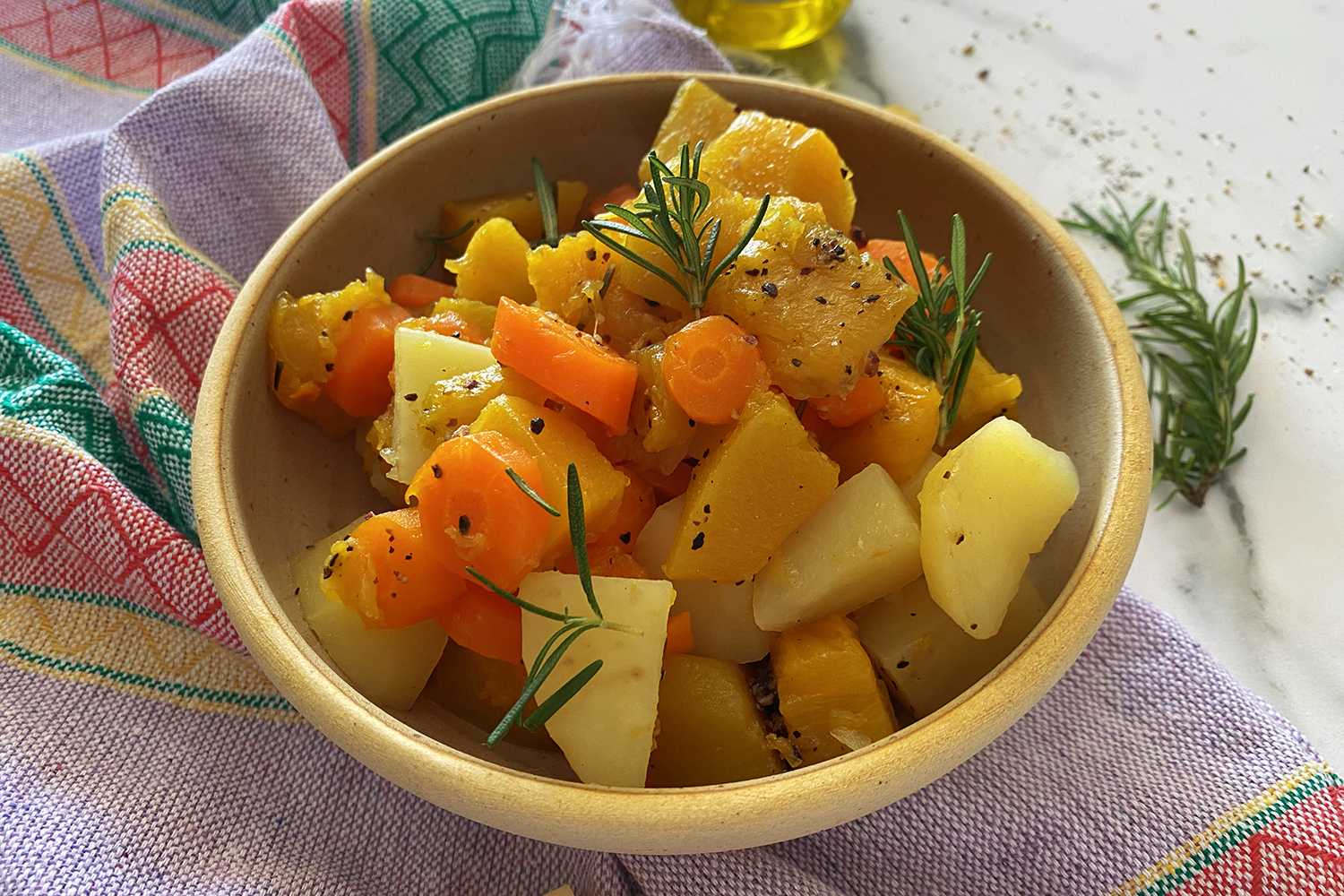Yellow bowl filled with carrot, potato and pumpkin cubes topped with rosemary sprig