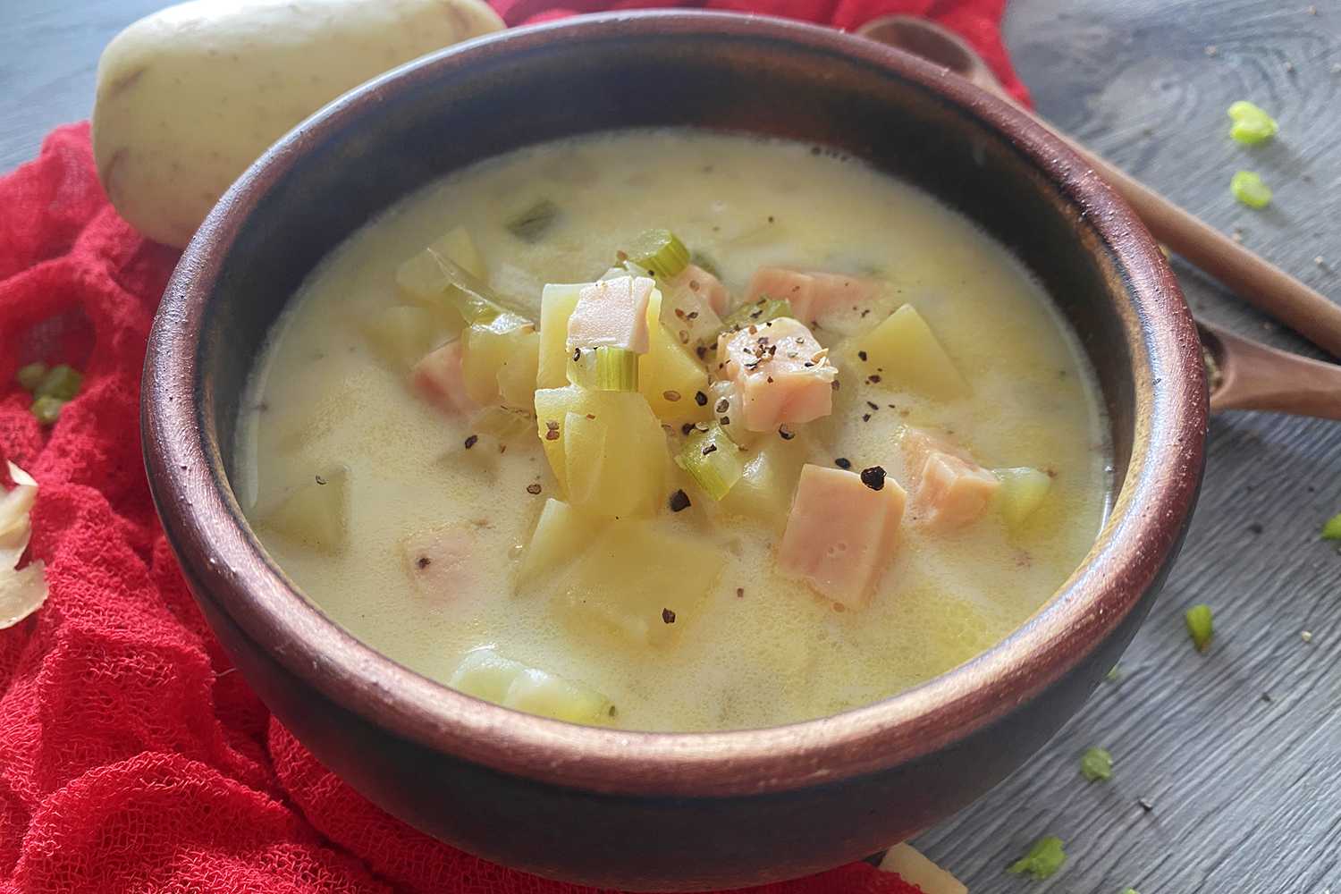 Yellow soup filled with ham cubes, potato cubes, celery and onion in brown bowl