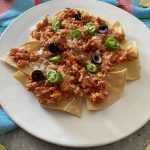 Nachos with ground beef with sauce topped with black ollives and chopped green chili