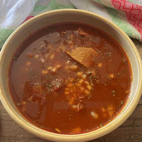 Rote Suppe mit Tortillas, Rindfleischstücken und Gewürzen