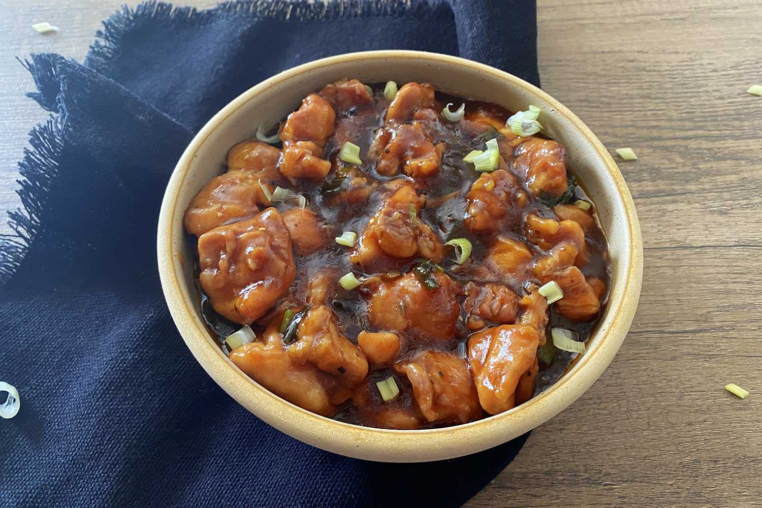 Chicken chunks in a brown sugary sauce with chopped scallion on top