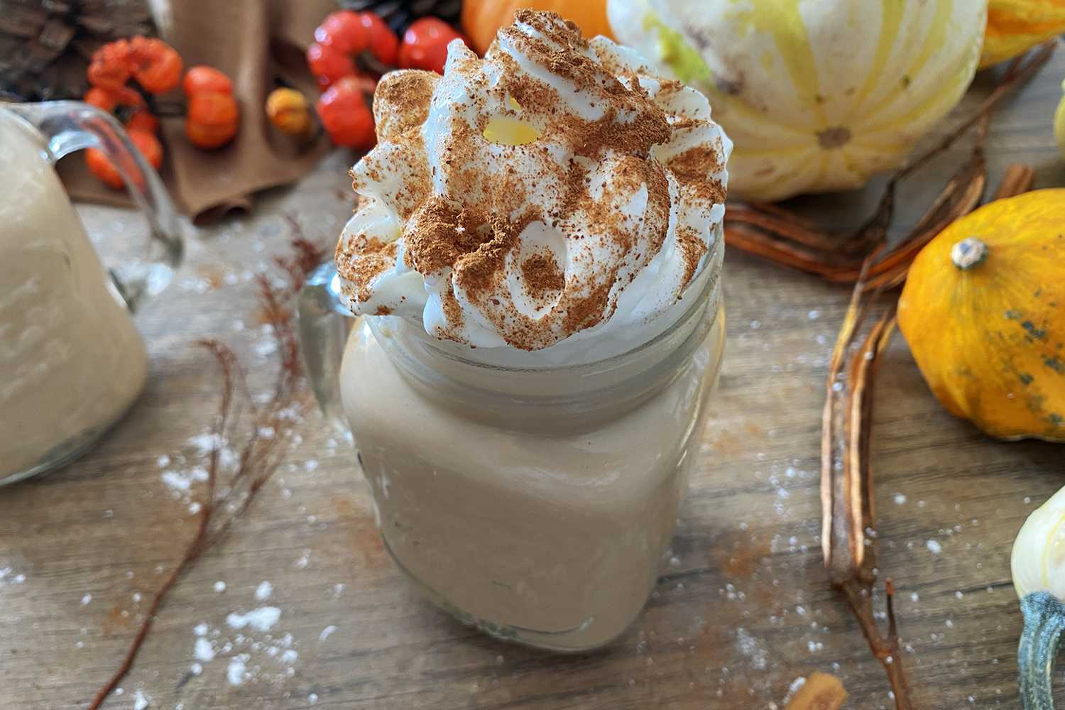 Pumpkin Spice Latte in a jar topped with whipped cream and cinnamon on a wooden table