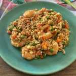 fried rice mixed with shrimp, peas and carrot cubes in a blue plate top view