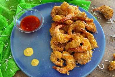 Fried shrimp coated with coconut on a blue plate with chili sauce on side