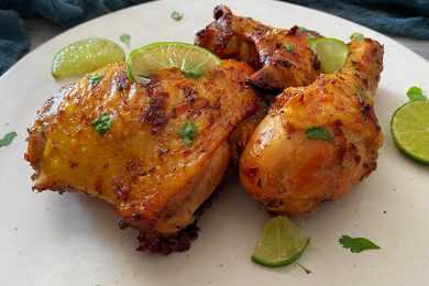 Roasted chicken thigh and chicken drumstick with spices, chopped parsley and lime slices on top