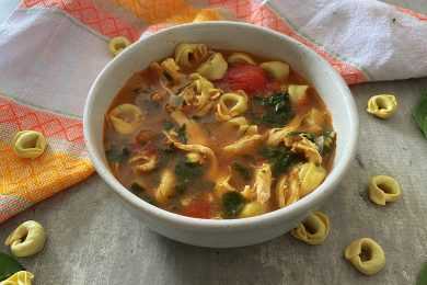 Red soup filled with tortellini noodles, tomato cubes and parsley