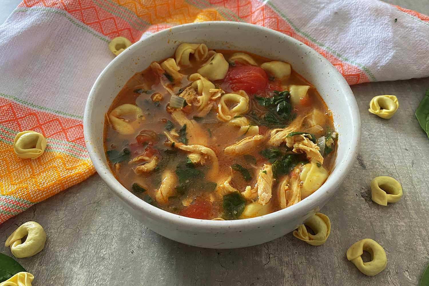 Red soup filled with tortellini noodles, chicken chunks, tomato cubes and parsley