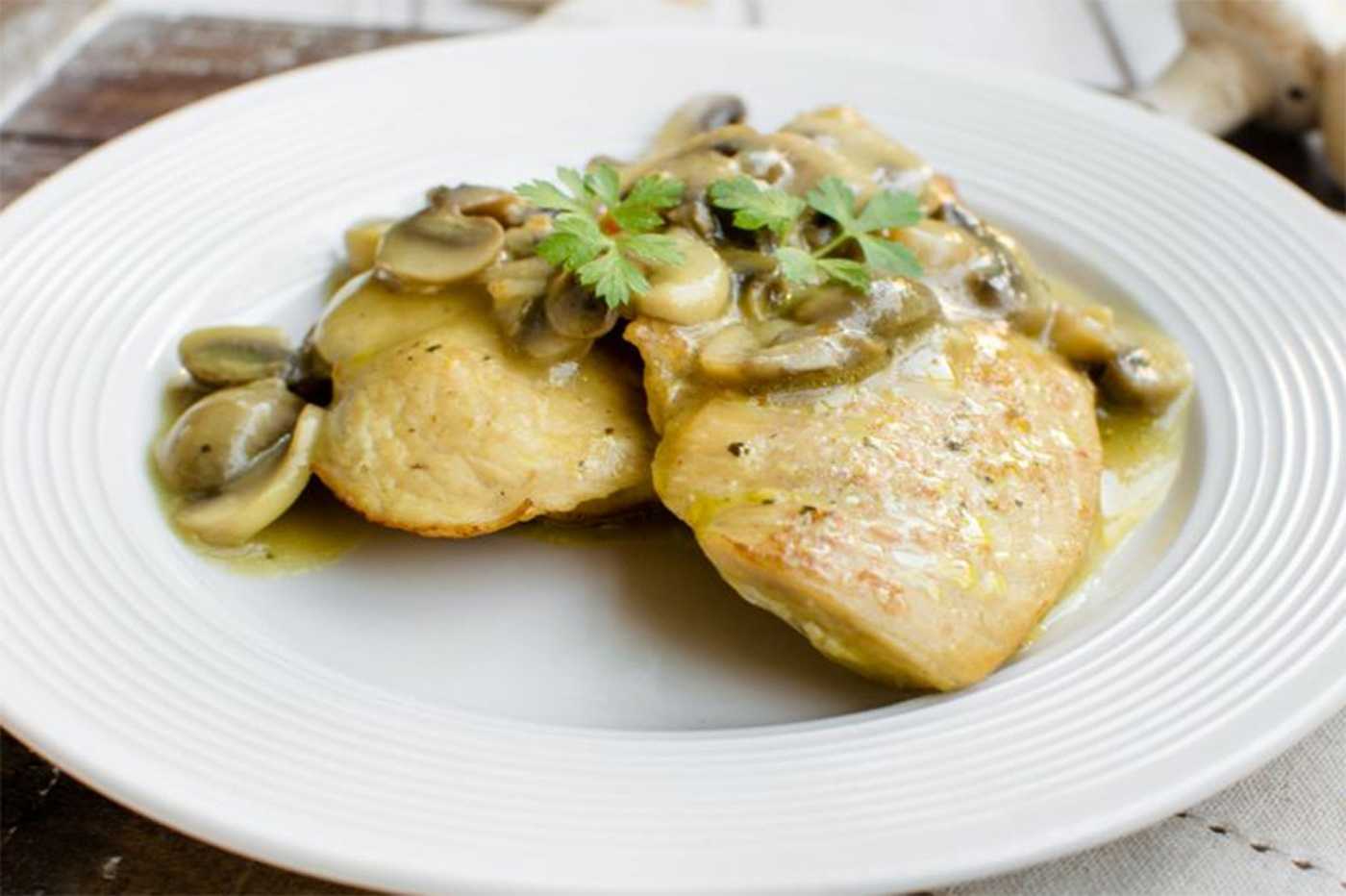 Chicken pieces with mushroom in mushroom sauce with parsley leaves on top over a white plate