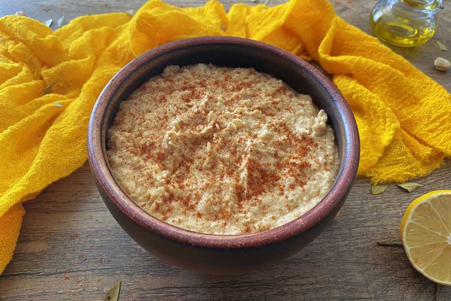hummus in a brown bowl topped with paprika with a lemon on side