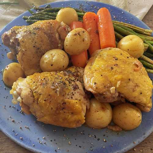 Hähnchenschenkel mit Karotten, Babykartoffeln und Spargel auf einem blauen Teller