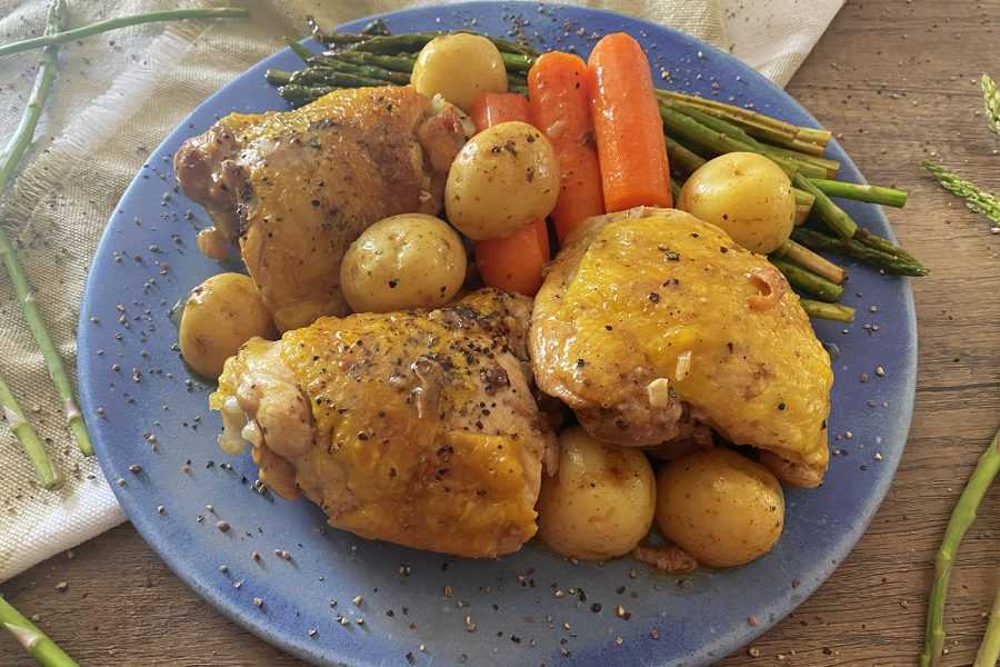 Hähnchenschenkel mit Karotten, Babykartoffeln und Spargel auf einem blauen Teller