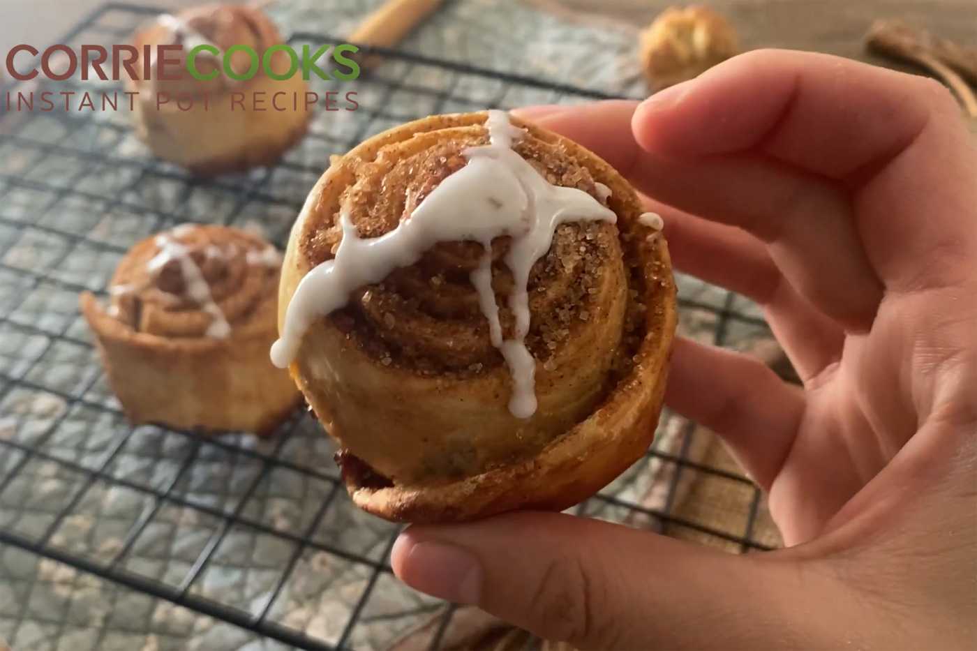 Hand holding cooked cinnamon roll topped with cinnamon and sugar and cream cheese