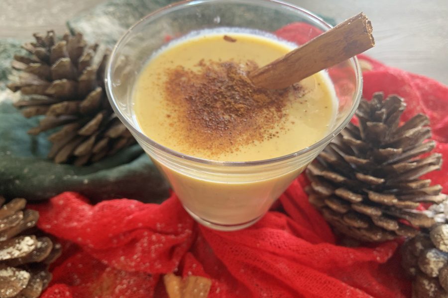 A glass filled with eggnog with cinnamon stick and pine cones on side