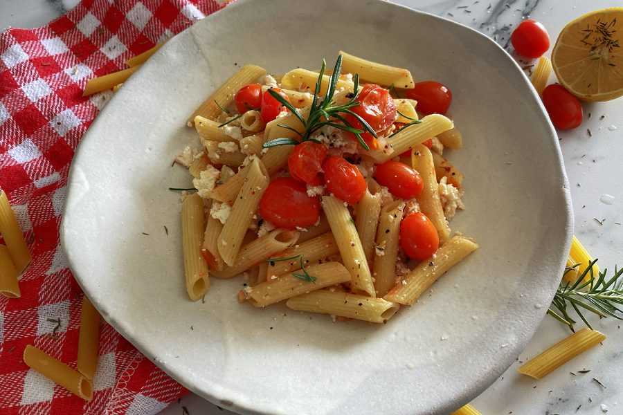 rigatoni pasta with cheese and cherry tomatoes in a white plate on a table