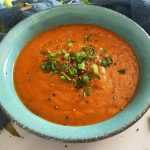 Tomato Basil Soup in a blue plate topped with green onion and pepper