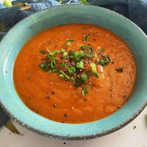 Tomato Basil Soup in a blue plate topped with green onion and pepper