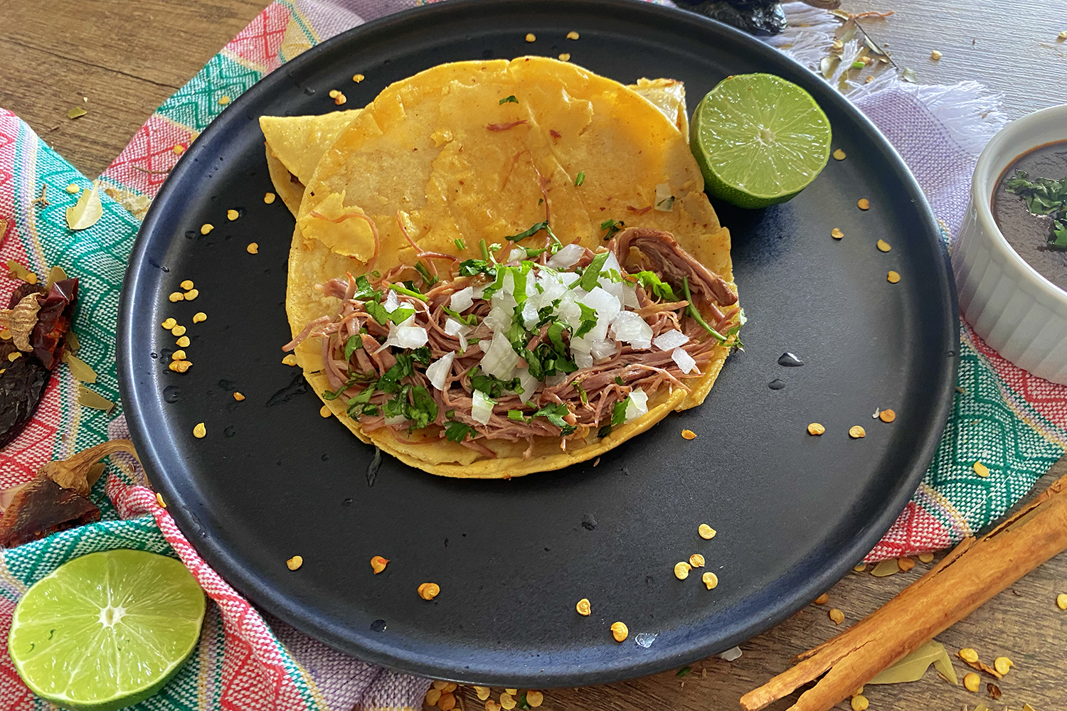 open birria taco filled with beef chunks, chopped onion and parsley on a black plate