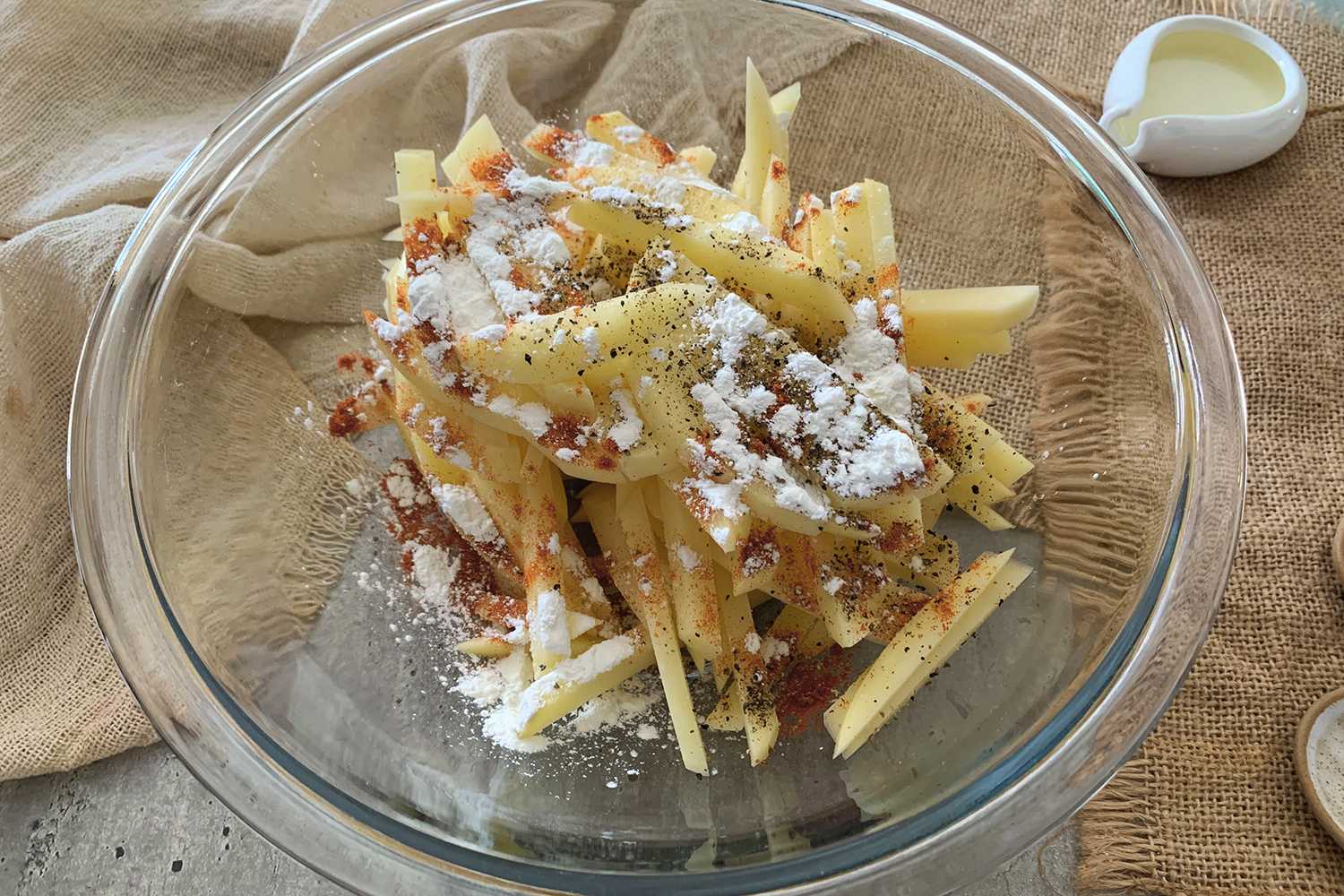 french fries sticks mixed with paprika, salt and pepper in a glass bowl