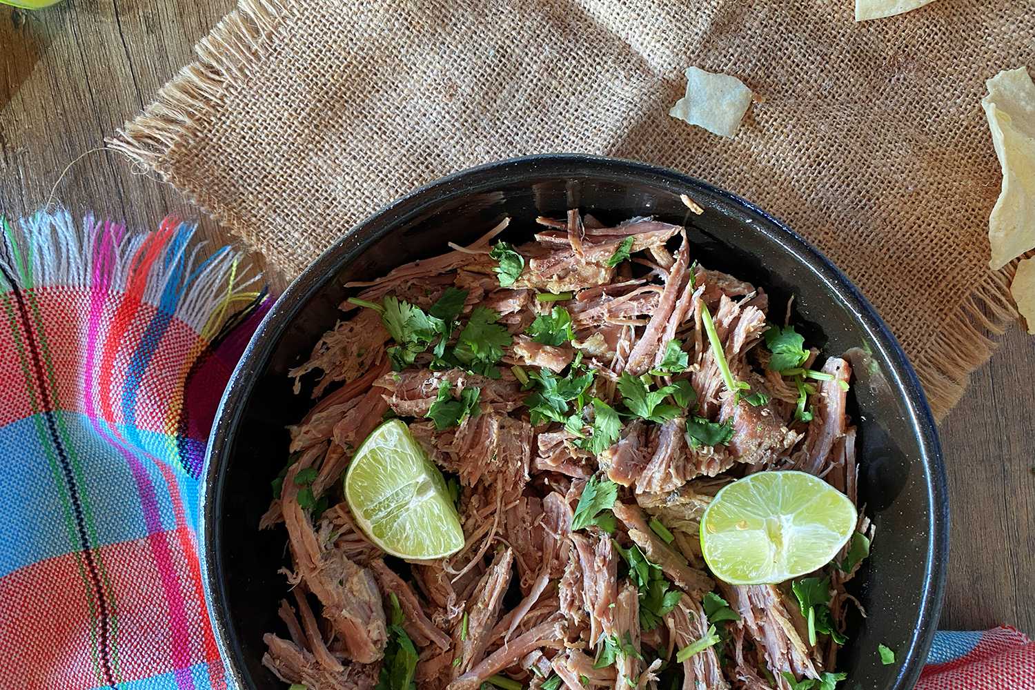 side view of a black bowl shredded meat with lime wedges 