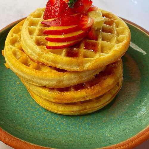 waffles in a plate topped with apple, strawberry and butter