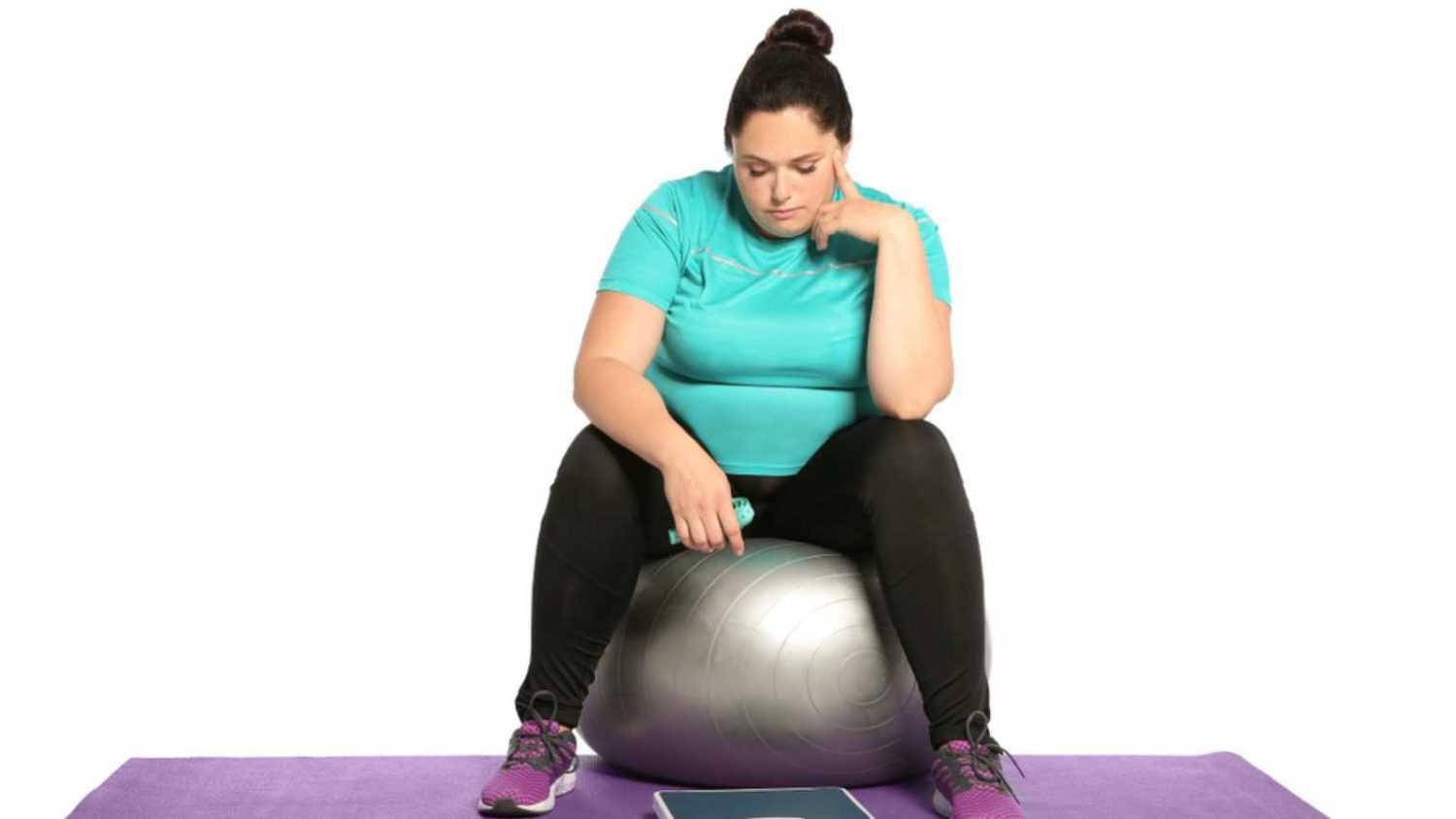 Upset overweight woman with scale, measuring tape and fitness ball on white background