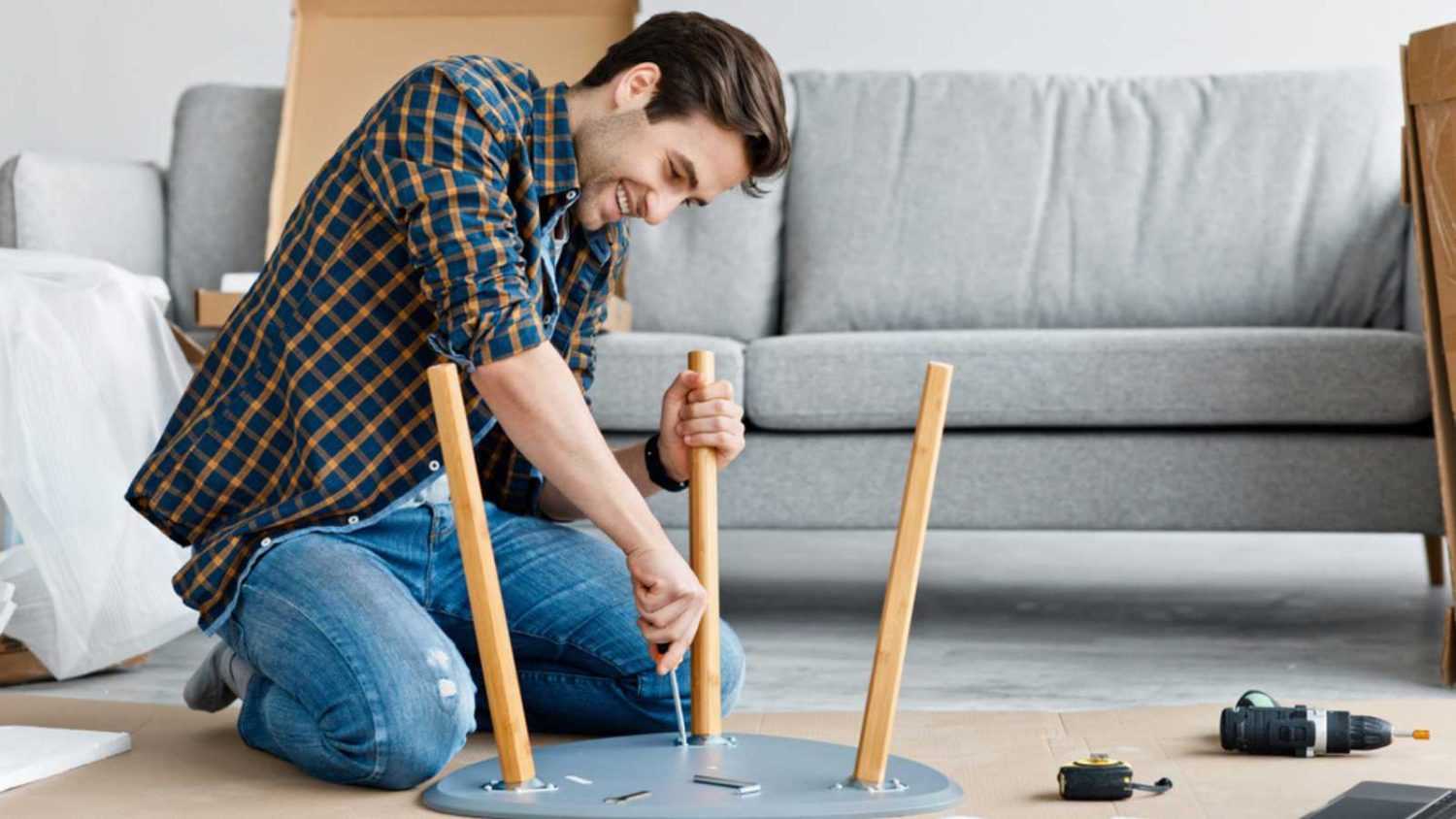 Furniture repair and assembly, handyman fixing table using tool, assembling at home after renovation. Happy millennial handsome guy screwing detail with screwdriver in living room interior, indoor