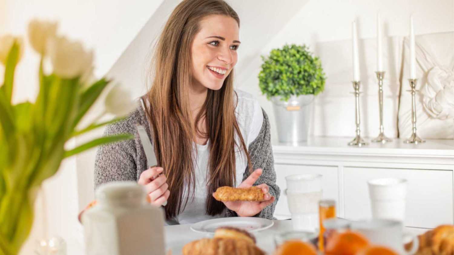 Young woman eating breakfast in the morning looking away to side with smile on face, natural expression.