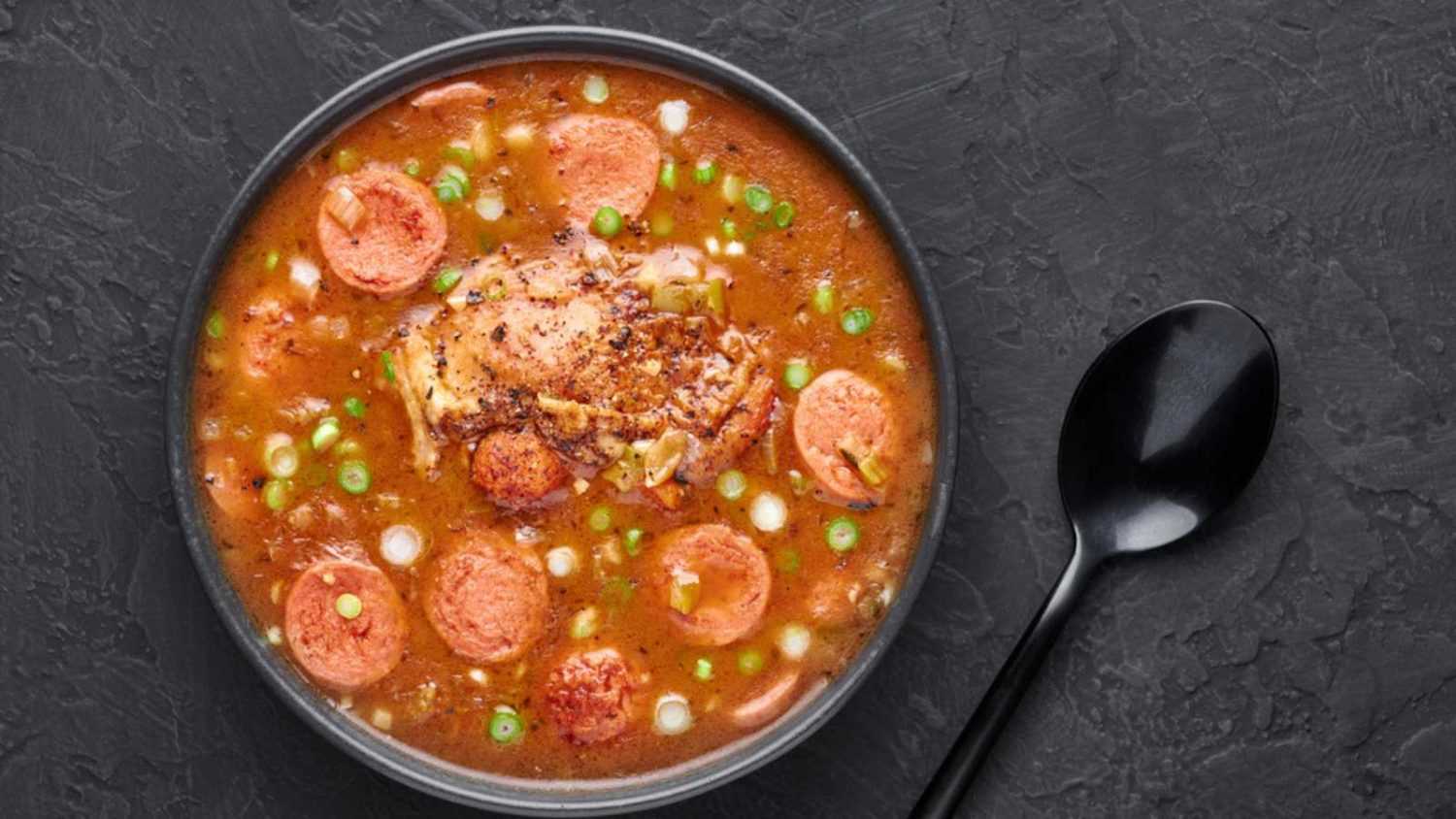 Chicken and Sausage Gumbo soup in black bowl on dark slate backdrop. Gumbo is louisiana cajun cuisine soup with roux. American USA Food. Traditional ethnic meal