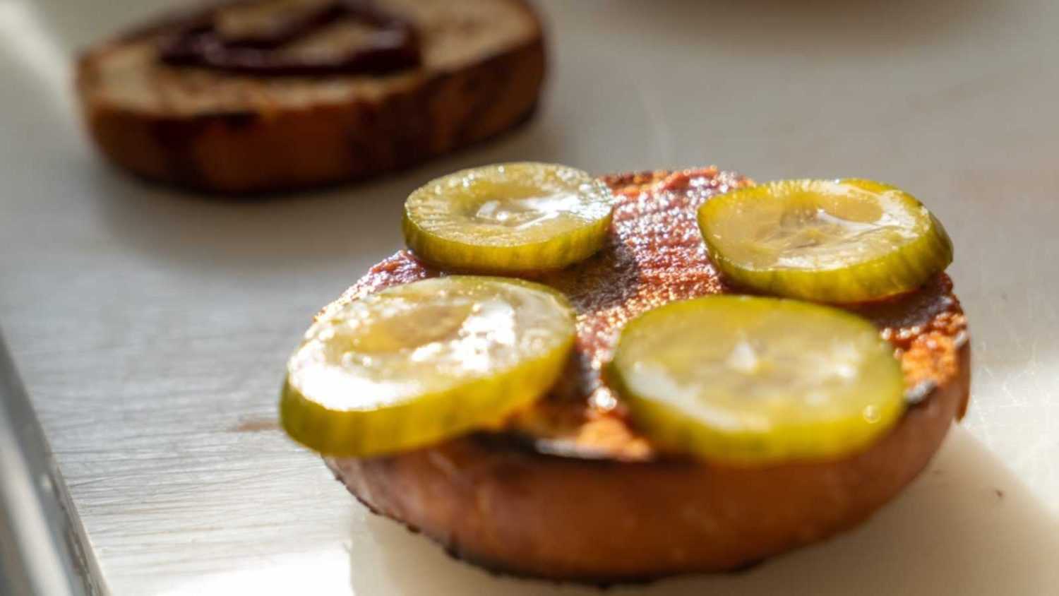 Round slices of pickles are placed on the ketchup-smeared hamburger bun. preparing a hamburger
