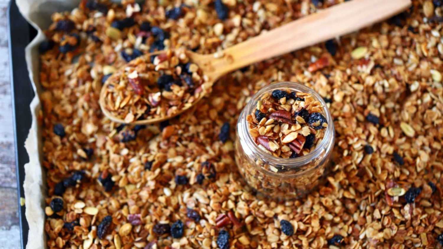 Freshly made homemade granola on a baking sheet. Granola in a wooden spoon and in a jar. Selective focus. Healthy diet concept. Keto diet.