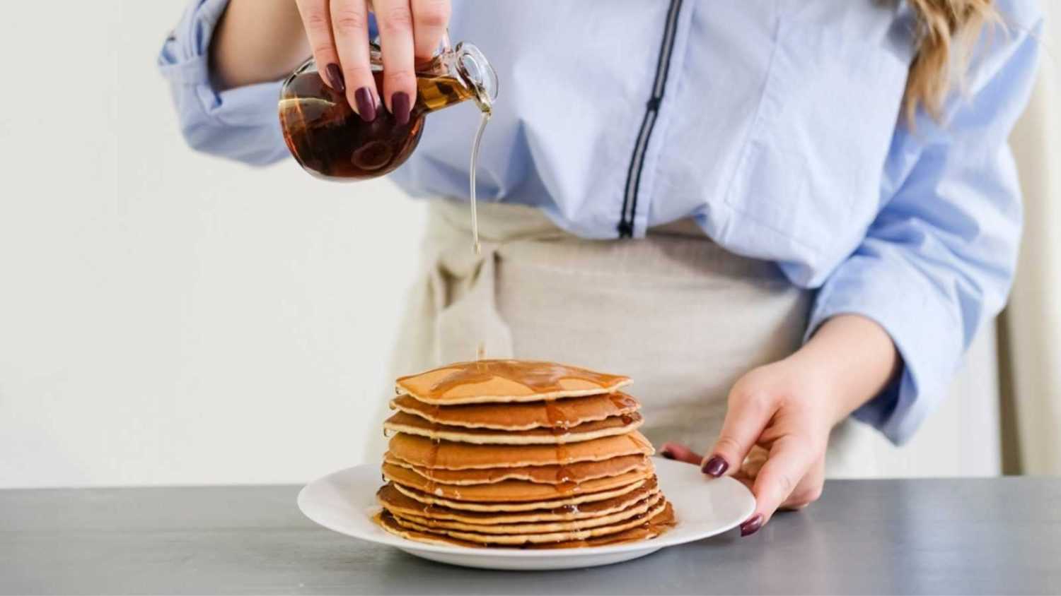 A woman pours pancakes with syrup. No face, close up. bright kitchen.