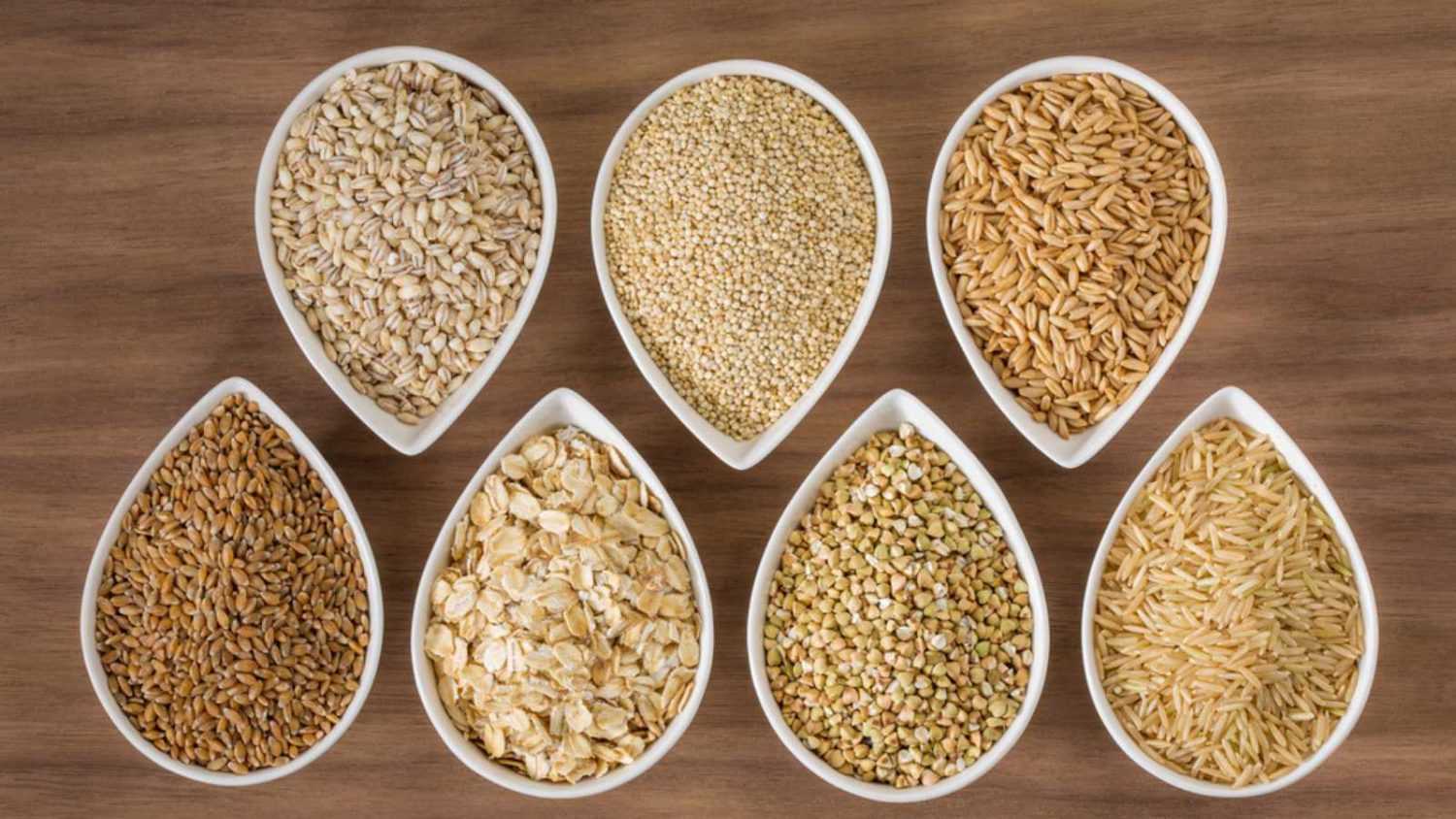 An assortment of whole grains in bowls over a wooden background