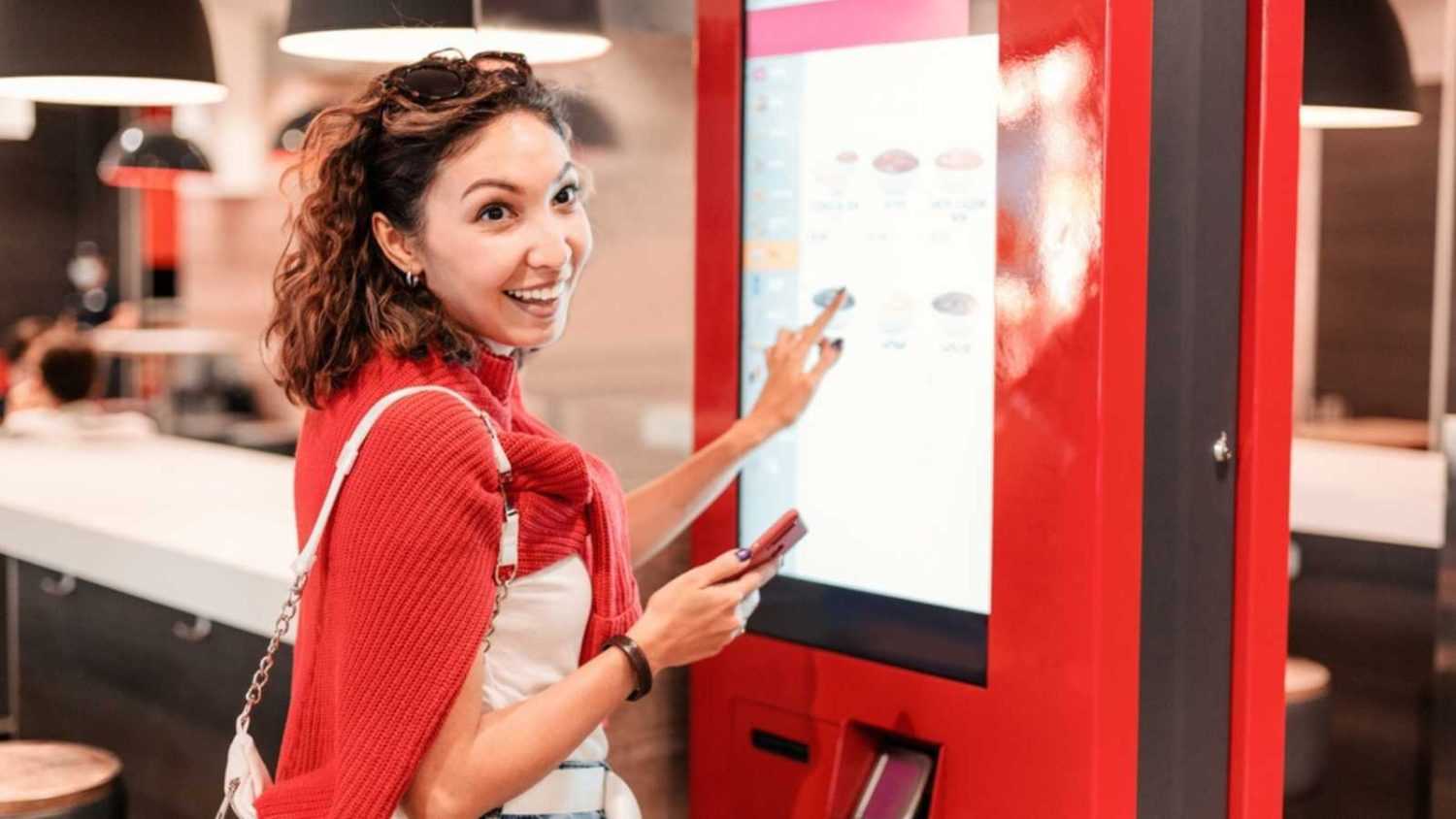 A girl orders food and lunch at a fast food restaurant using a self-service kiosk or a terminal with a screen. Modern commerce equipment