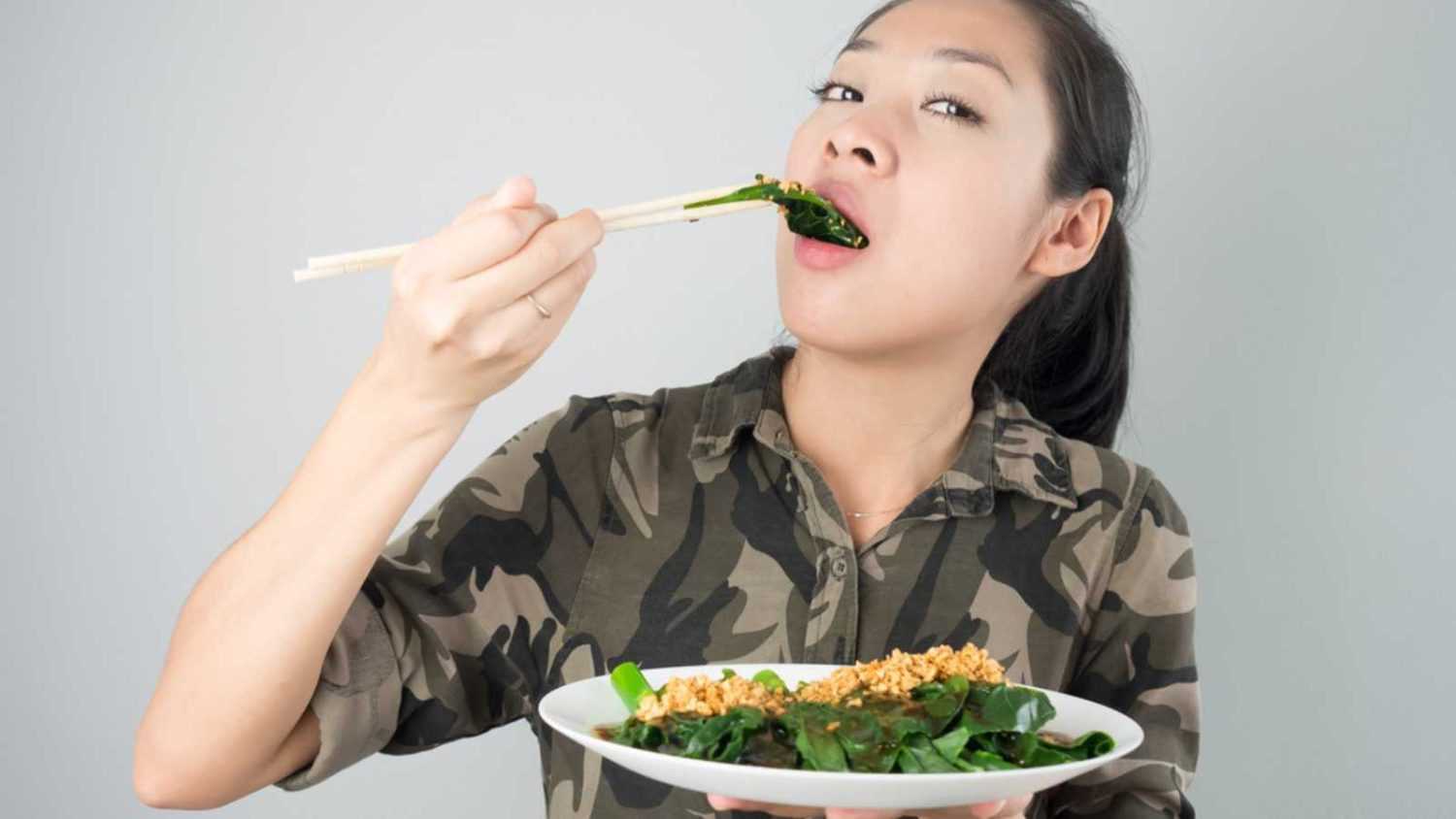 Asian woman eating kale fried in oyster sauce.