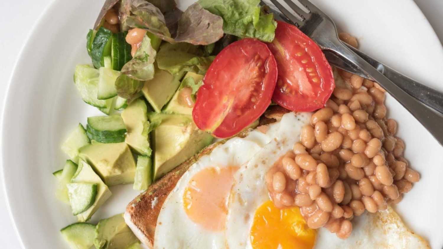 High angle closeup of homemade vegetarian brunch plate, including eggs, avocado, beans, tomato, salad, lettuce