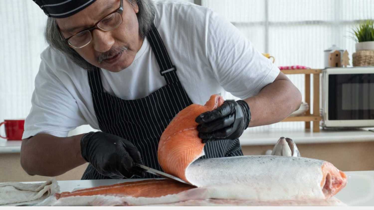 Senior chef use sharp knife slicing raw fresh salmon fillet for sashimi and sushi in modern kitchen