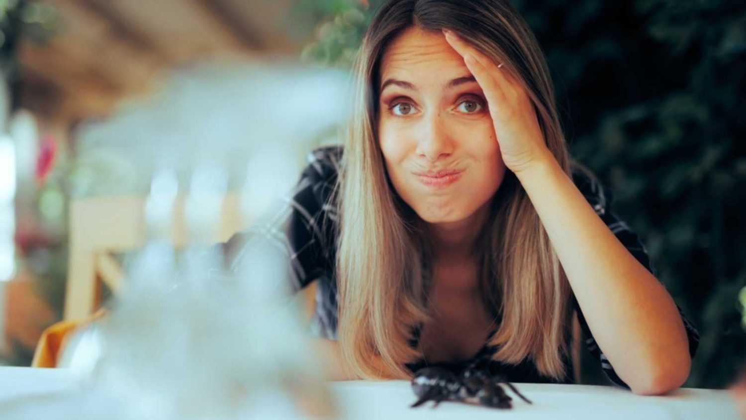 Unhappy woman at restaurant finding insect on table