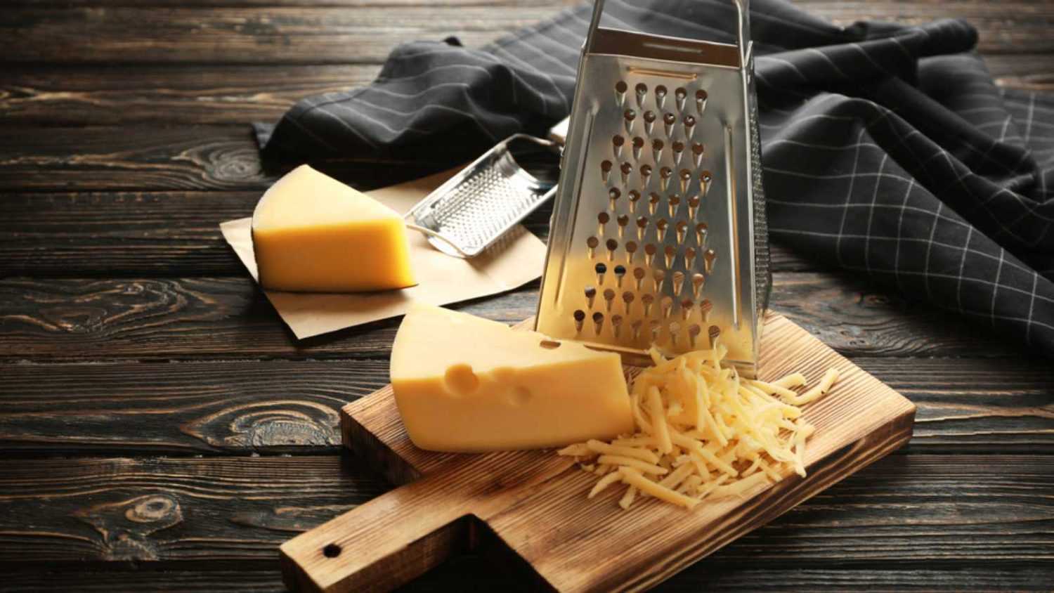 Grater and cheese on wooden board