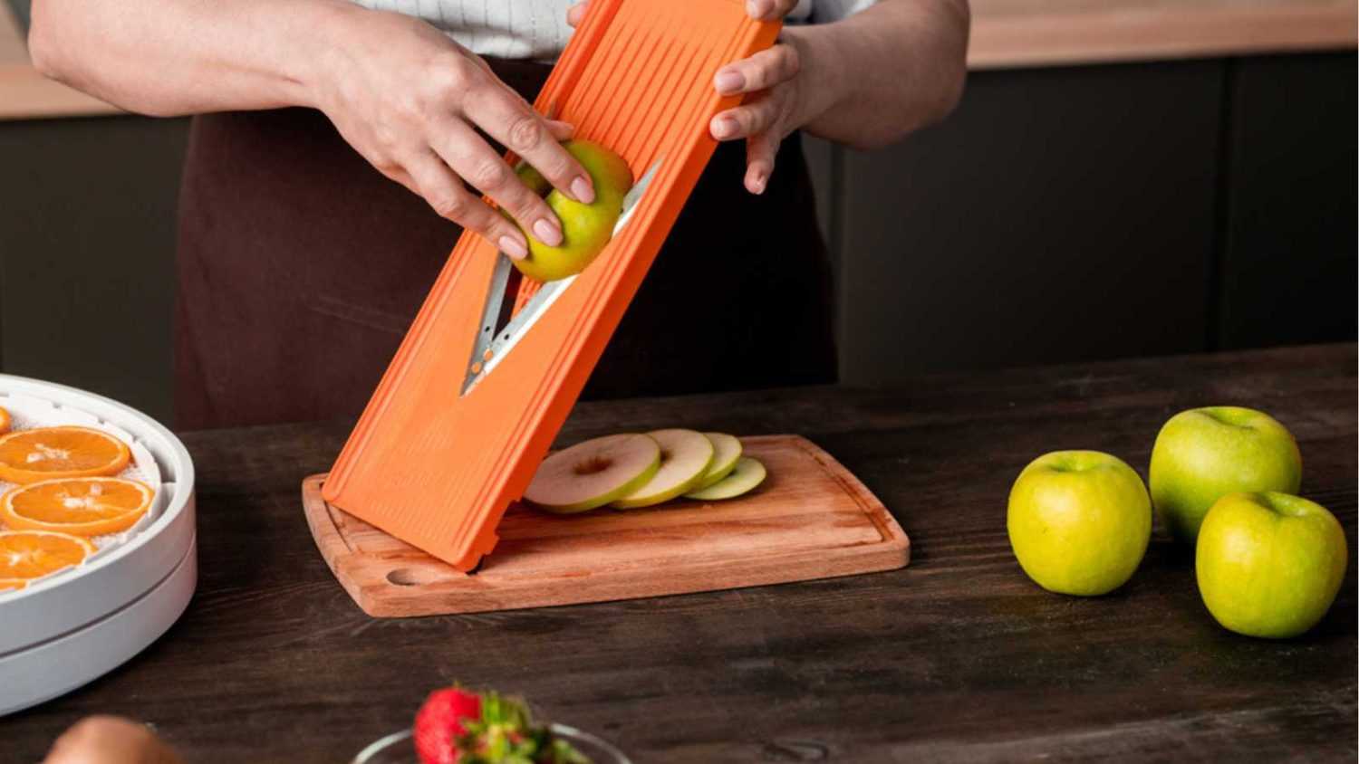 Close-up of unrecognizable woman using mandoline slicer for cutting apple while preparing fruits for dehydration at home