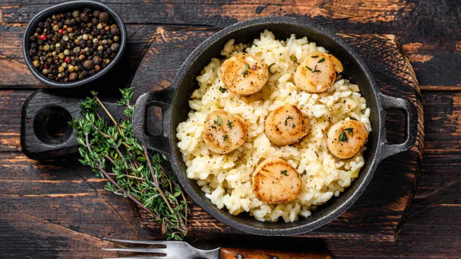 Seafood Risotto with Scallops in a pan. Dark wooden background. Top view