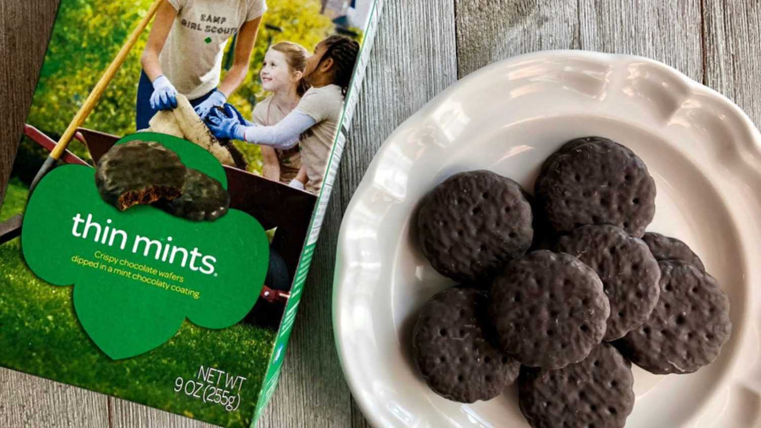 Box of Girl Scout Thin Mints with a few on a white plate on a wooden surface