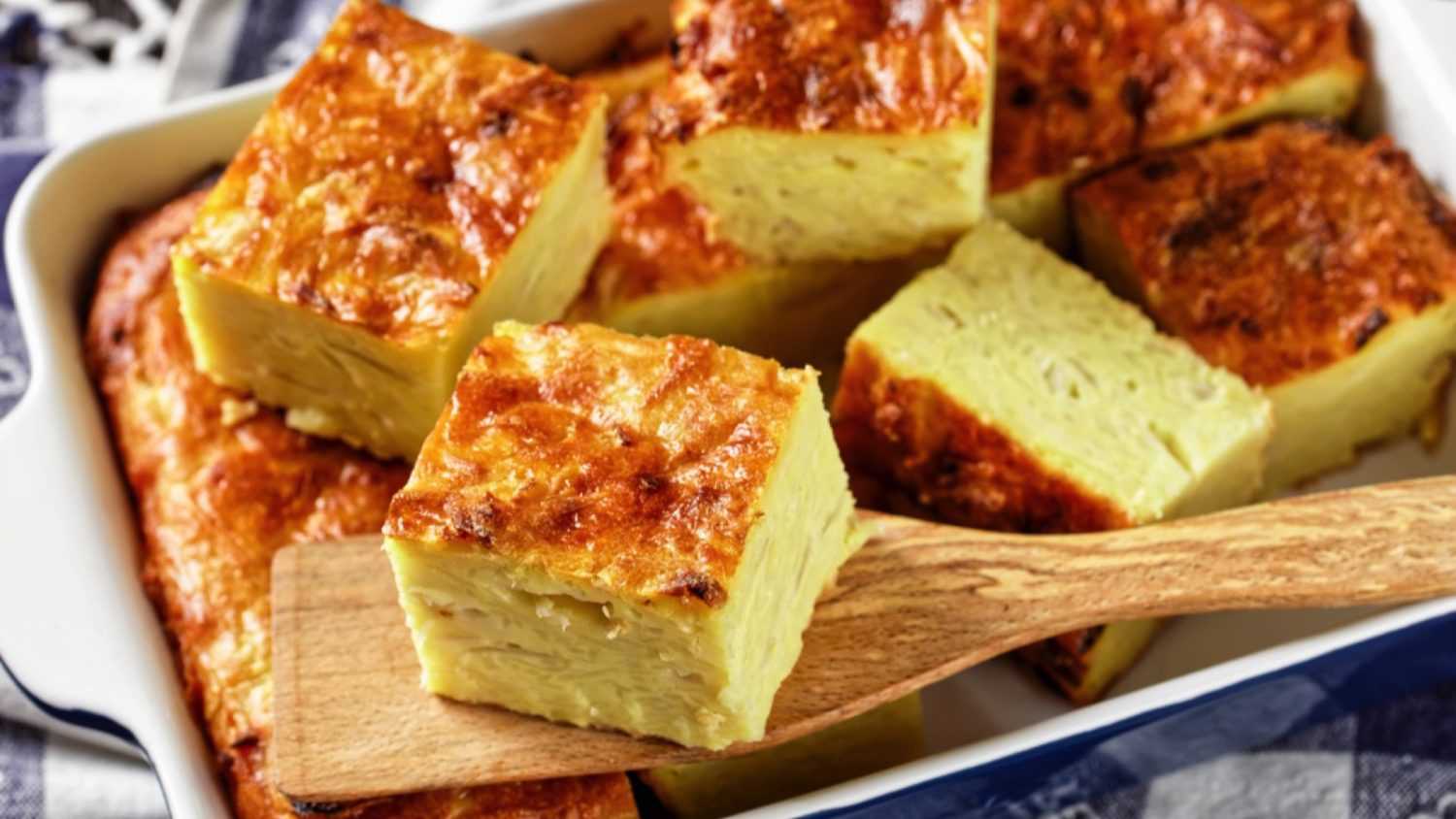 potato kugel, baked pudding or casserole of grated potato cut in portions in a baking dish on a wooden table, jewish holiday recipe, close-up