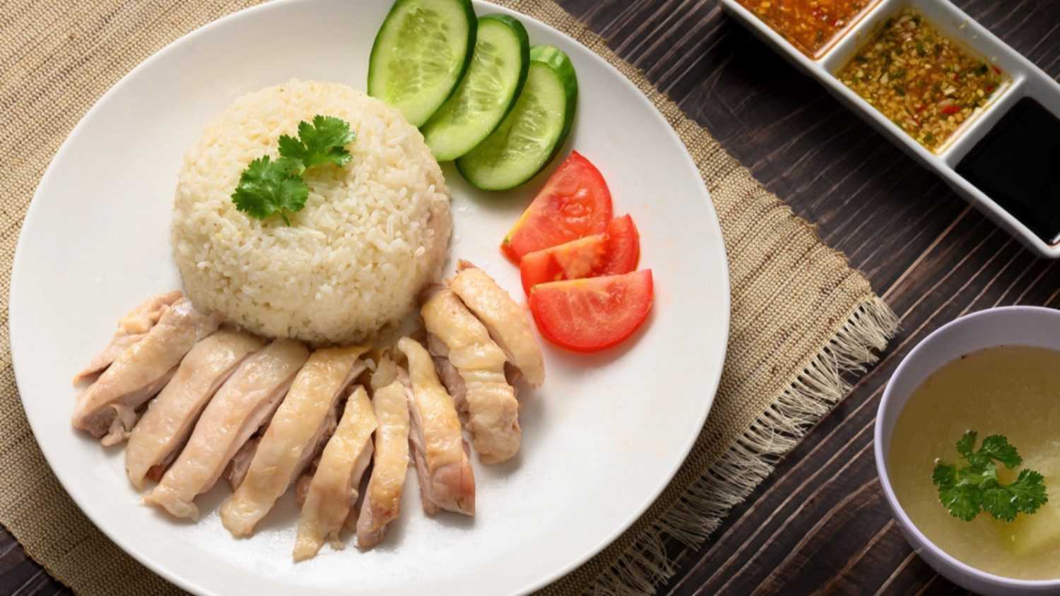 Hainanese chicken rice with soup and three sauces on dark wood table texture