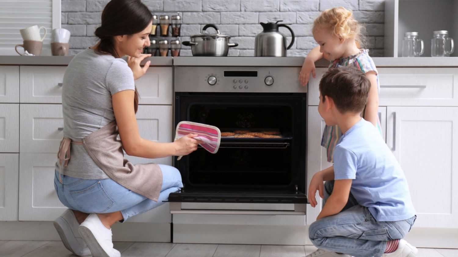 Little kids watching their mother bake cookies in oven