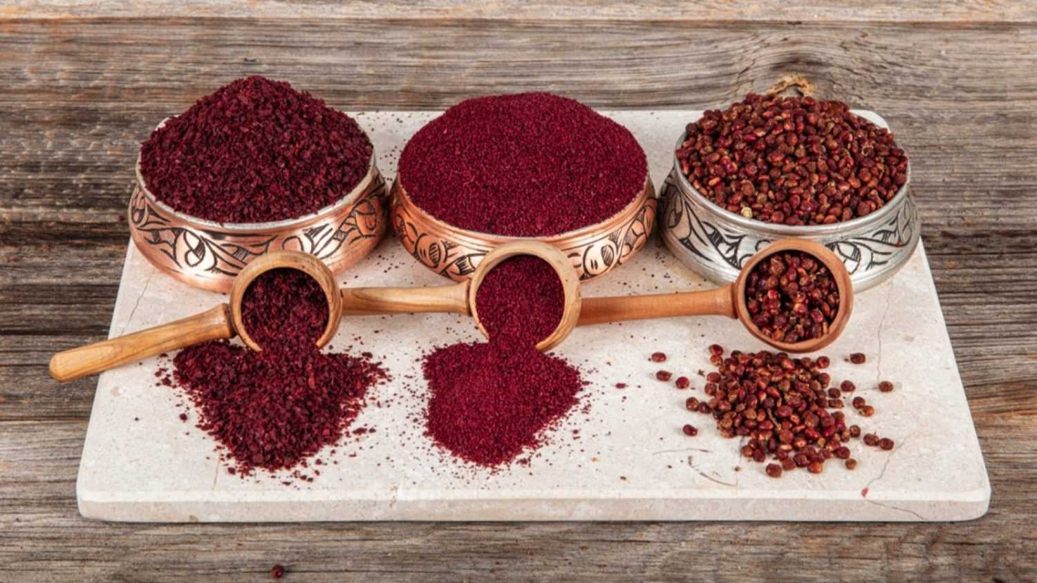 Dry spice sumac in a wooden spoon. Ground sumac spice. Dried ground red Sumac powder spices in wooden spoon with sumac berries on rustic table. Healthy food concept.